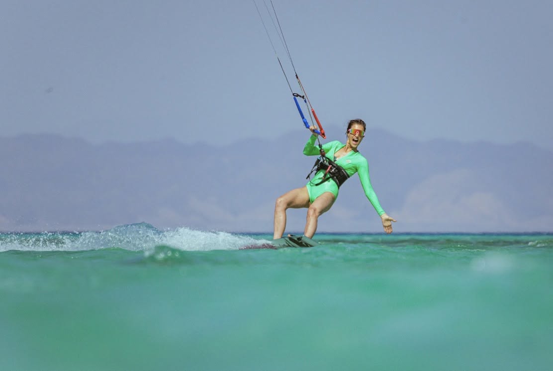 A kitesurfer in a bright green suit riding across turquoise water