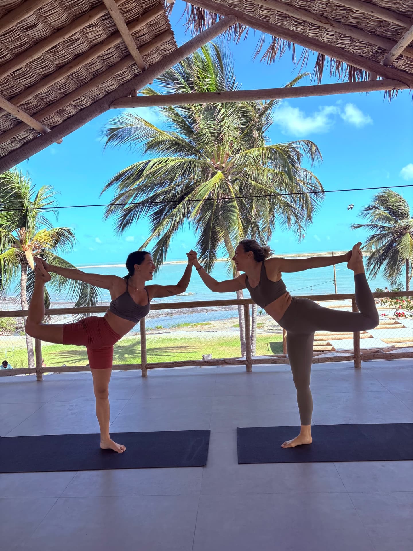 Two guests holding hands while balancing in dancer pose during an open-air yoga session