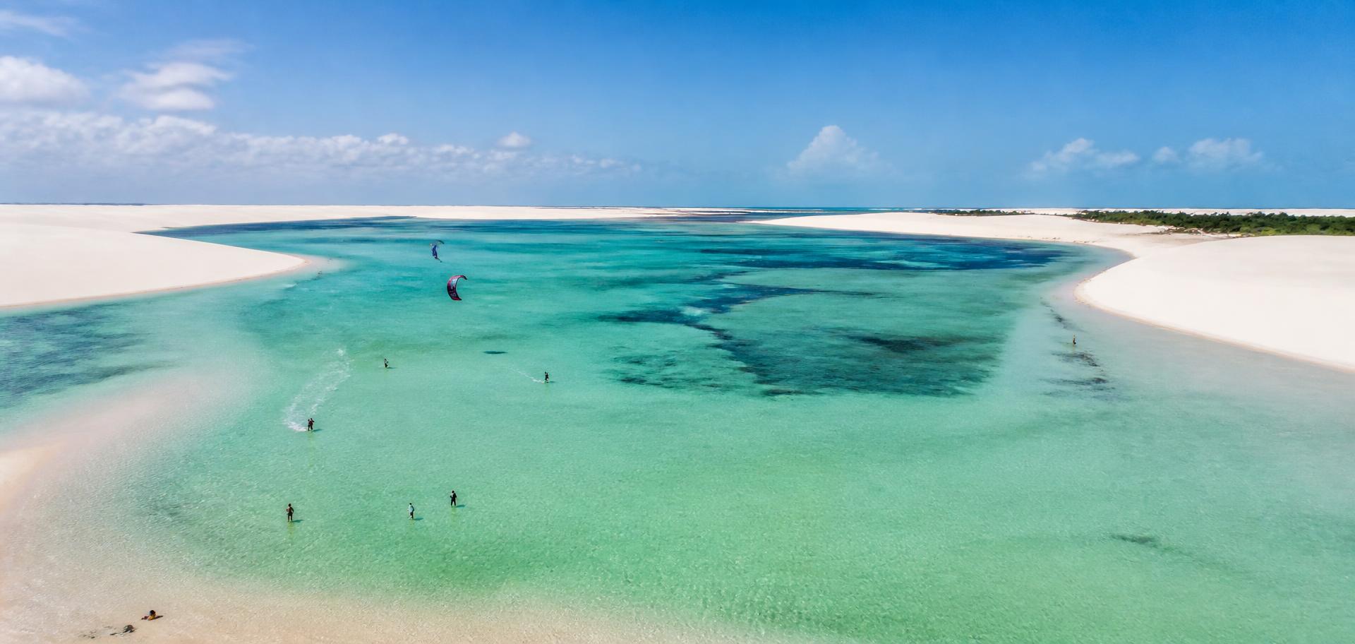 Aerial view of a turquoise lagoon between white sand dunes with kitesurfers