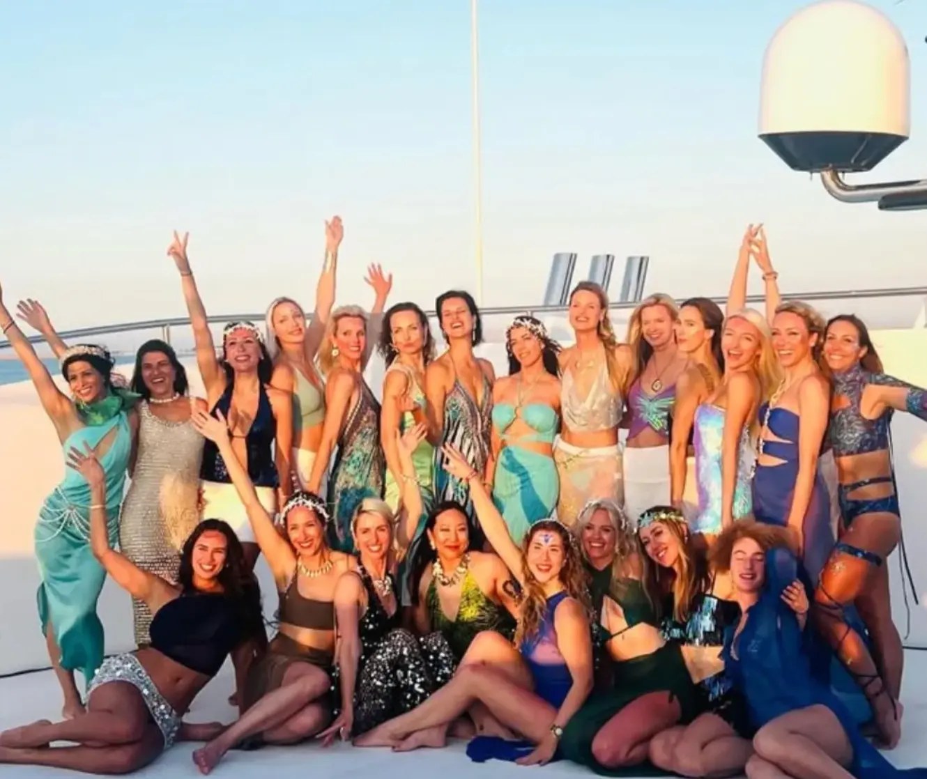 The whole crew dressed up on deck at golden hour, arms in the air