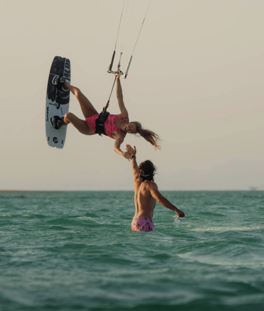 Rider boosting a jump and high-fiving a friend standing in the water